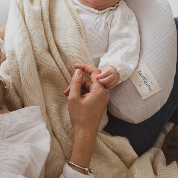 Baby liegt auf Bio-Stillkissen und greift nach der Hand seiner Mutter